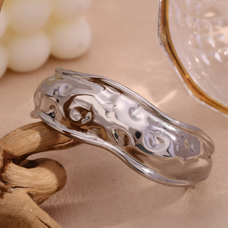 Bracelet manchette sculptural en acier inoxydable argenté à surface ondulée et brillante.