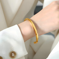 Bracelet rigide fin en titane plaqué or, design lisse et brillant, porté au poignet féminin.