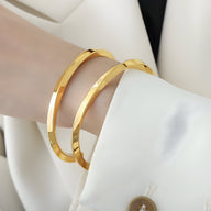 Bracelets jonc simples en titane plaqué or, finition brillante et bords arrondis, portés au poignet féminin.