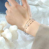 Bracelet triple mailles en titane plaqué or avec motif croix délicat, porté au poignet féminin.