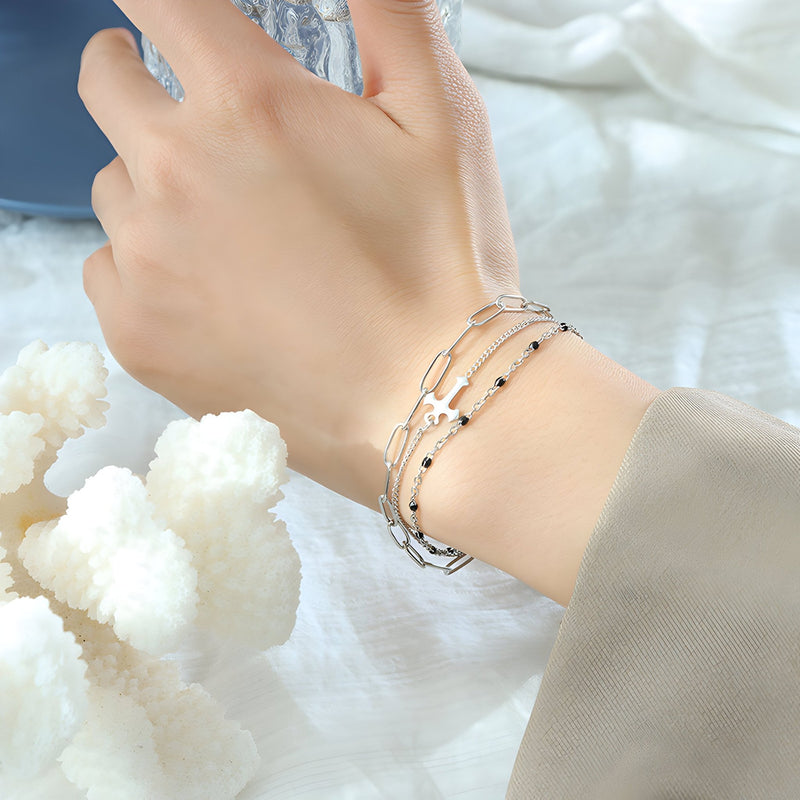 Bracelet triple mailles en titane plaqué or avec motif croix délicat, porté au poignet féminin.