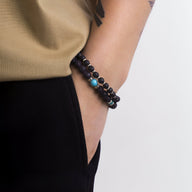 Ensemble de deux bracelets pour homme en pierres volcaniques noires avec perle turquoise et détails métalliques dorés.