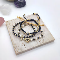 Trio de bracelets noirs à perles et strass dorés avec pendentif cœur en strass noir et blanc.